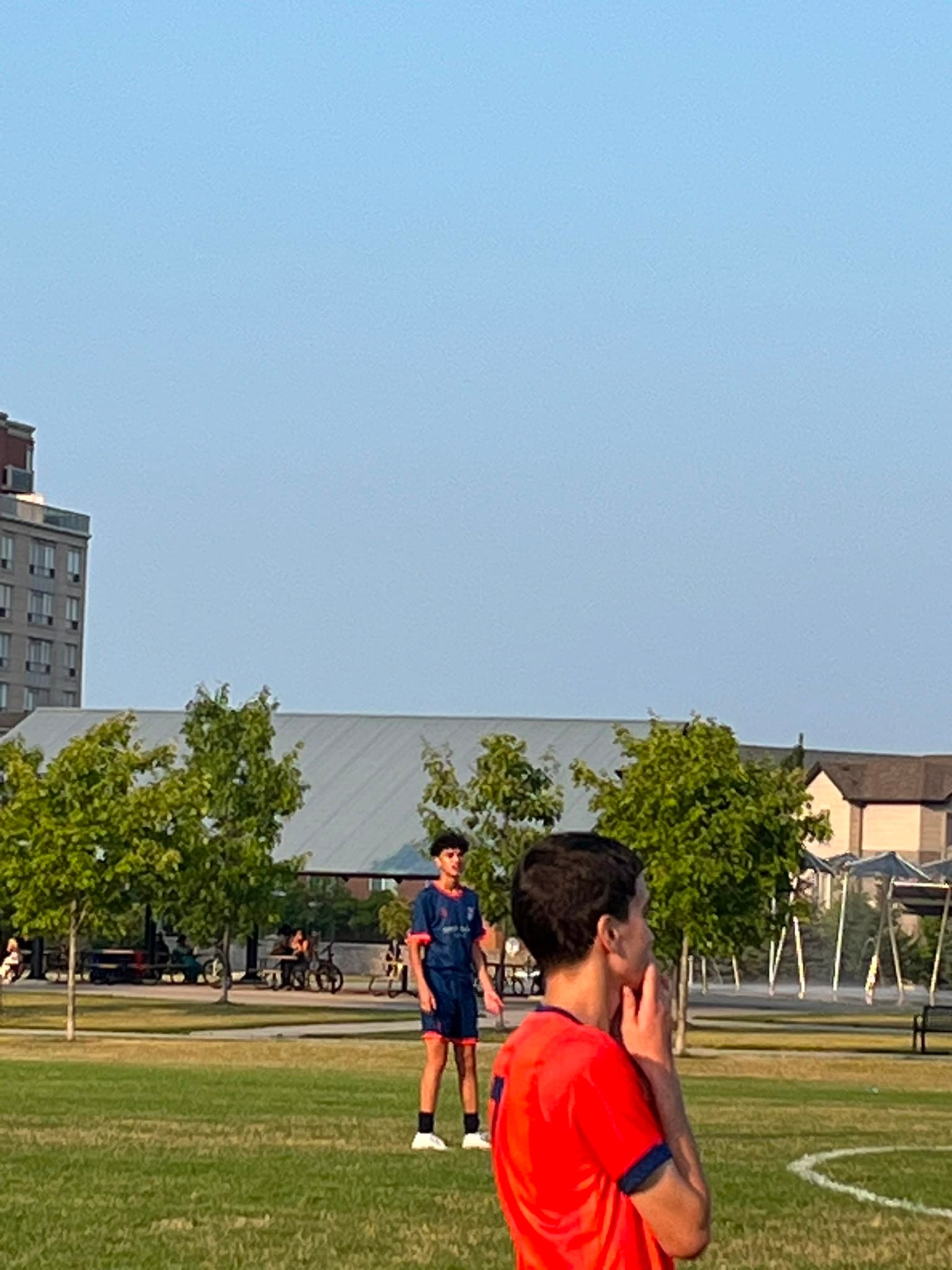 Two young footballers pause on a grass field in a Toronto park