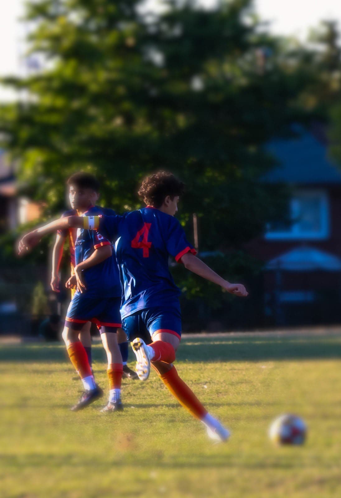 A young player in navy and orange kit moves across a Toronto grass field in golden-hour light