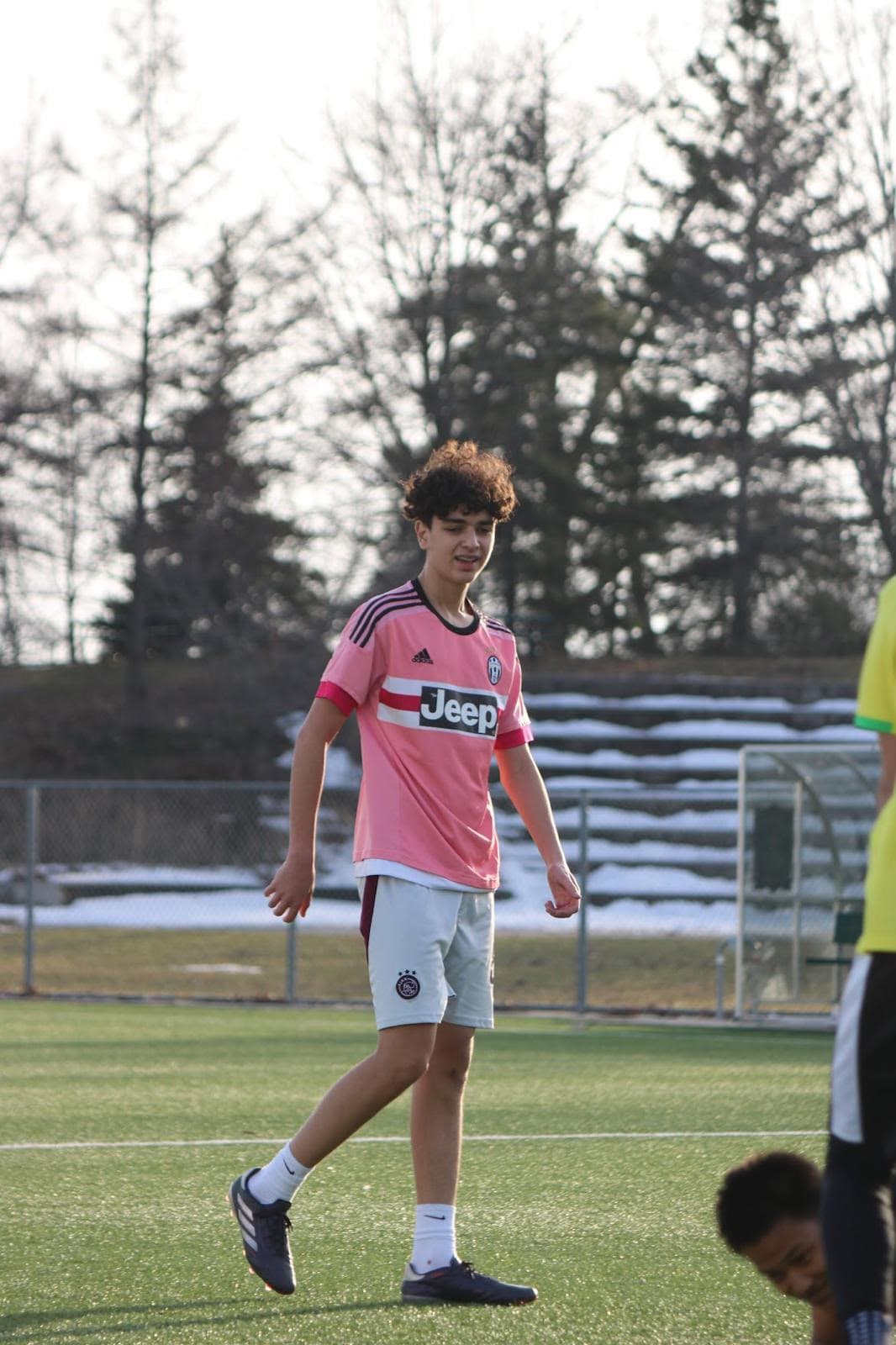 A young player in a pink training top walks across an artificial turf pitch in Toronto